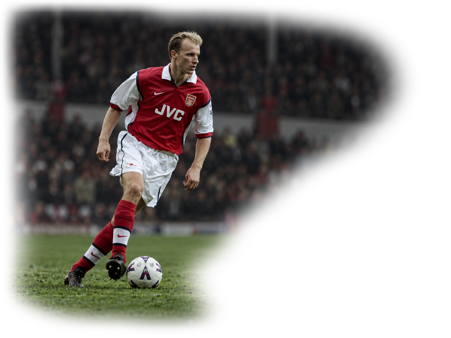 Football player dribbling on the grass in a crowded stadium